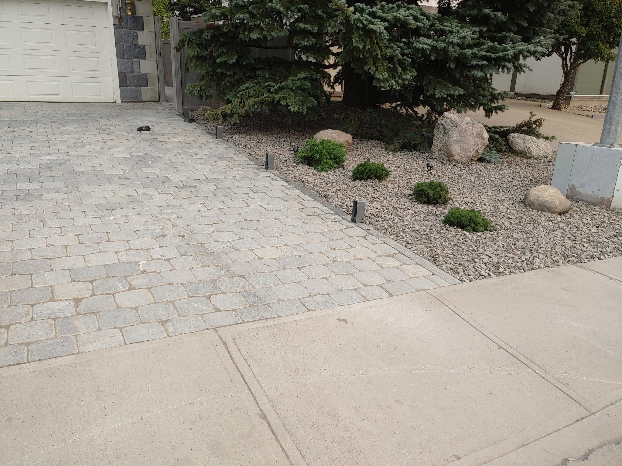 Paver driveway with cobblestone-style blocks and shrub landscape bed